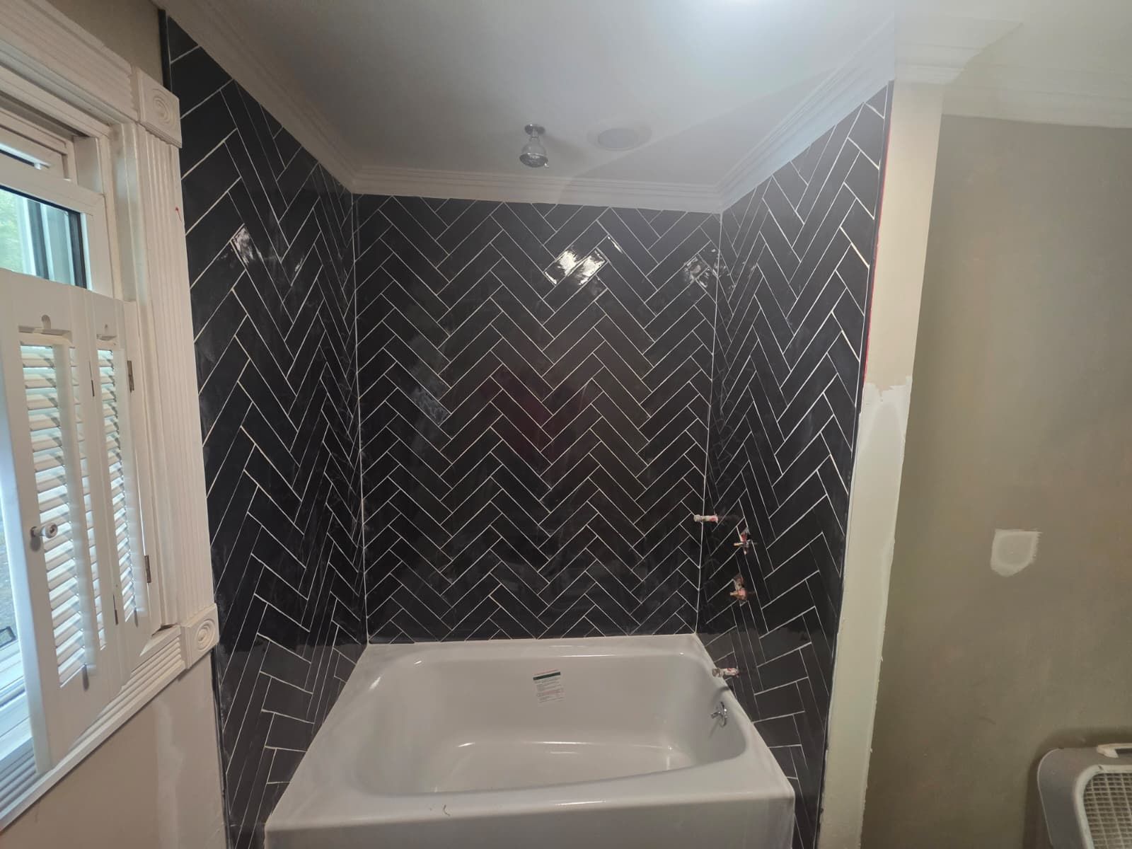 Bathroom with a white tub and black herringbone tile surround next to a window.
