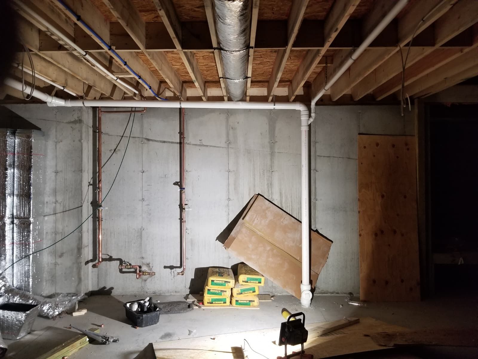 Dim unfinished basement with exposed ceiling beams, scattered debris, and stacked boxes against a concrete wall