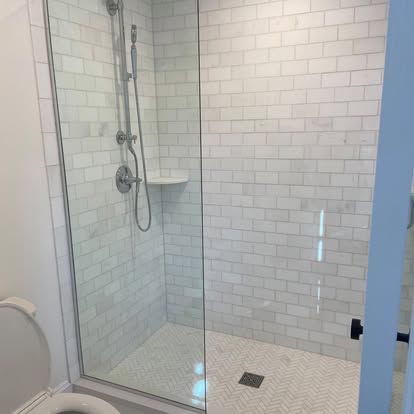 Glass-enclosed walk-in shower with white subway tile, chrome fixtures, and a built-in corner shelf.