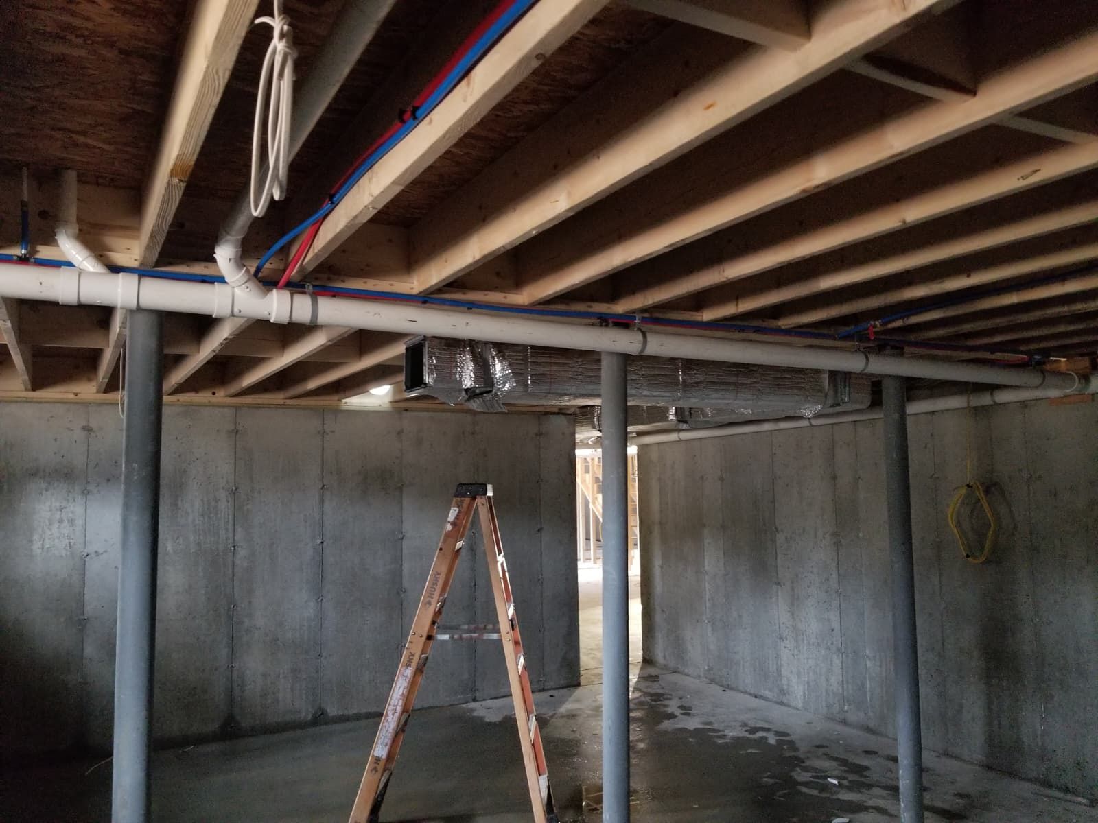 Basement under construction with exposed ceiling beams and a ladder in the center