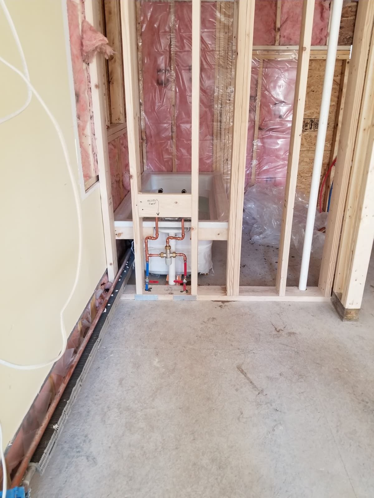 Unfinished room wall framing with exposed plumbing, insulation, and a concrete floor