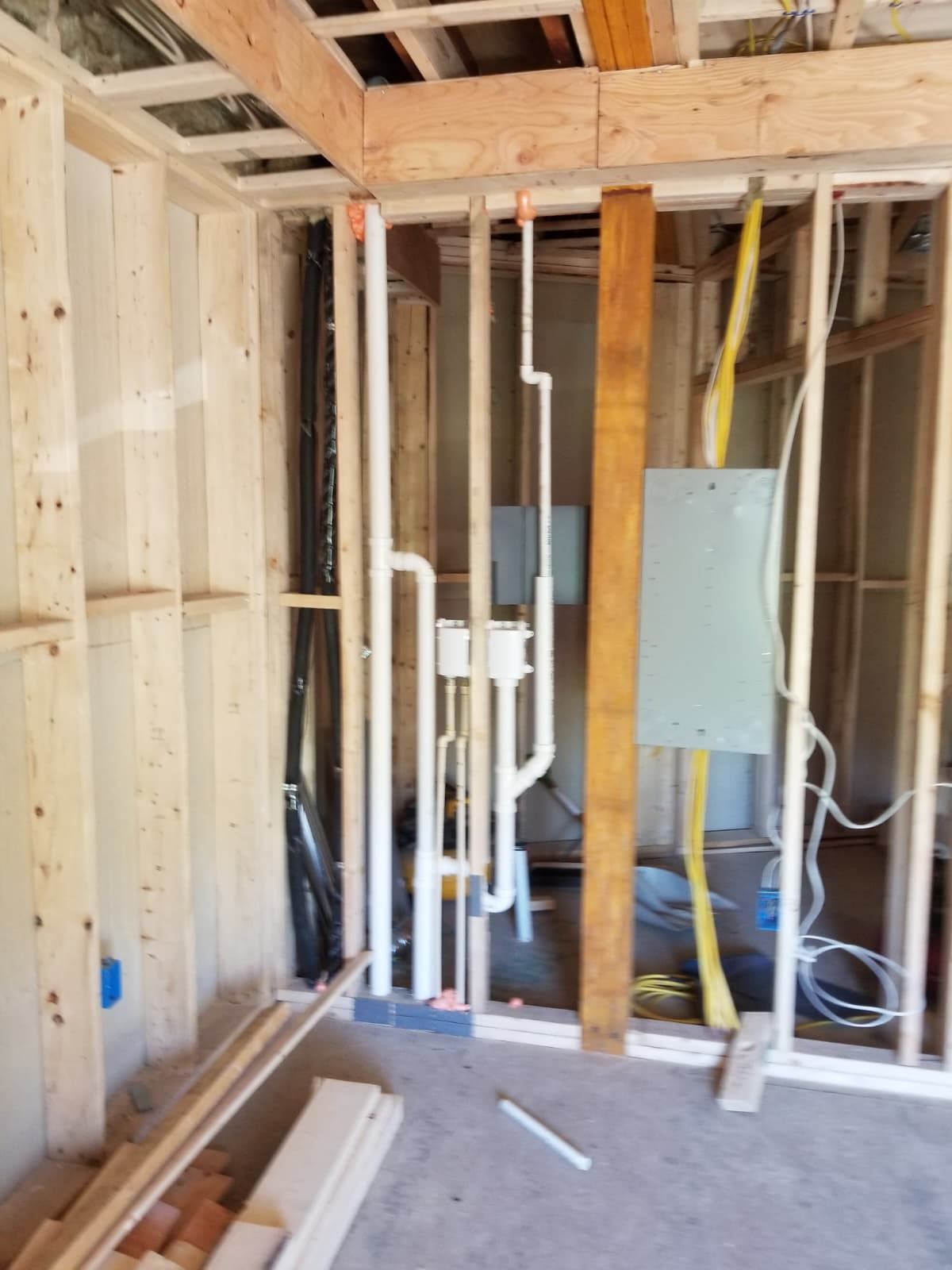 Unfinished room framing with exposed pipes, electrical boxes, and drywall panels in a construction site