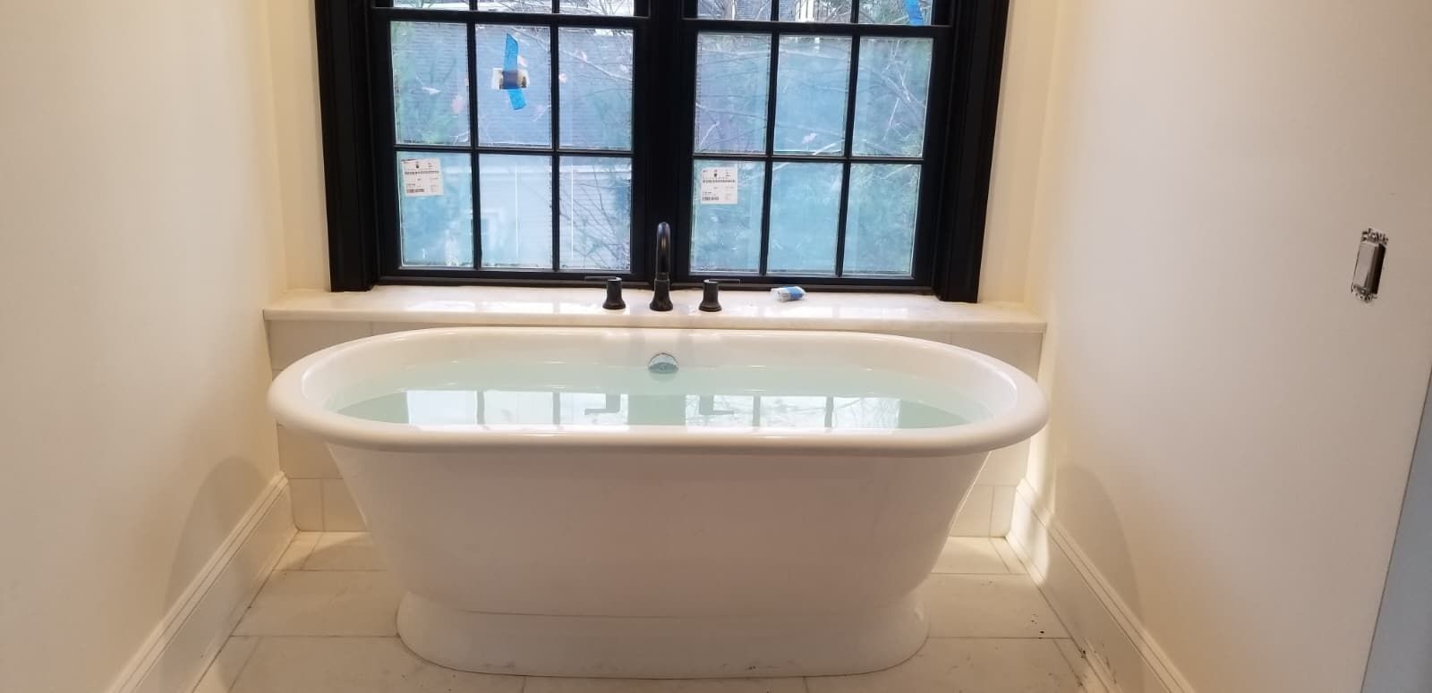 White freestanding bathtub centered below a window in a small bathroom alcove