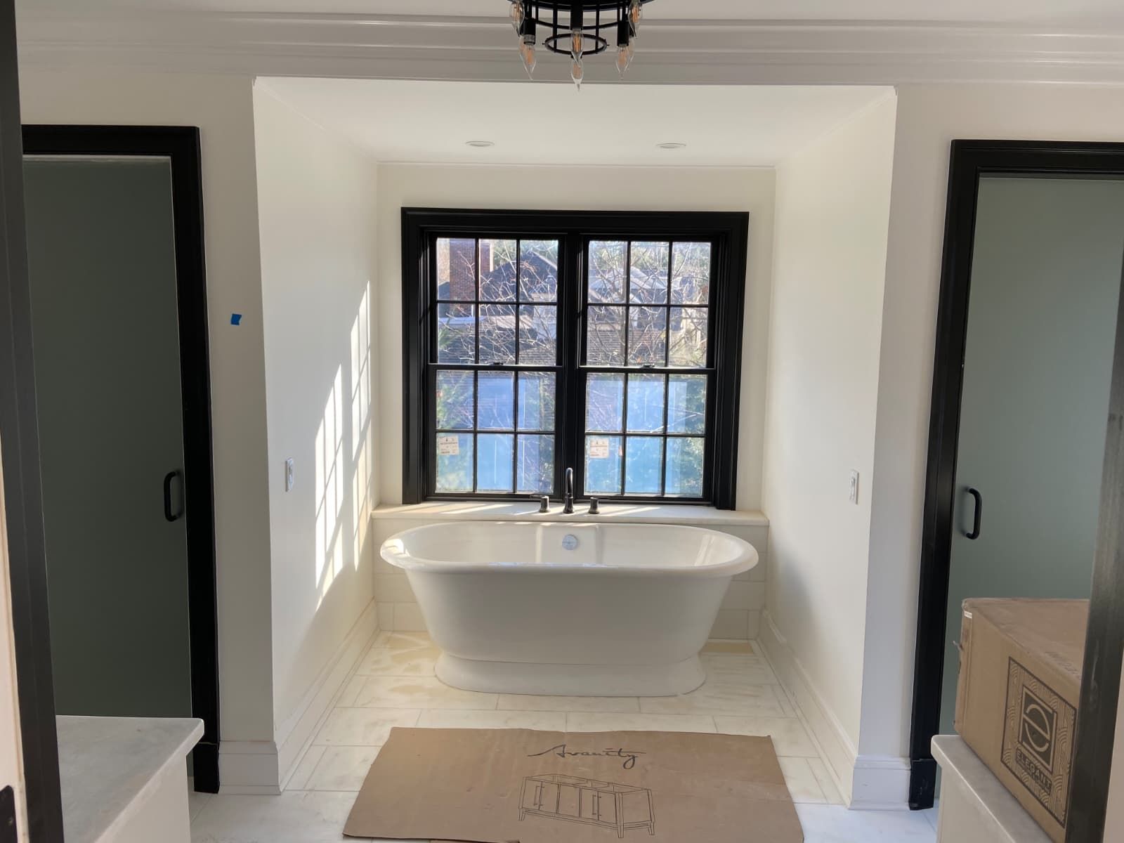 Bright bathroom with a white soaking tub beneath a black-framed window and mirrored doors on both sides