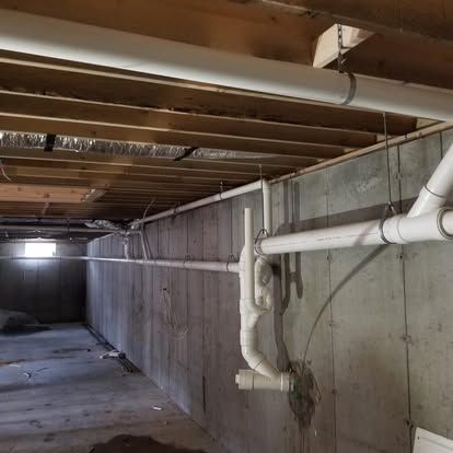 Concrete basement crawlspace with exposed wooden joists and white PVC pipes along the wall
