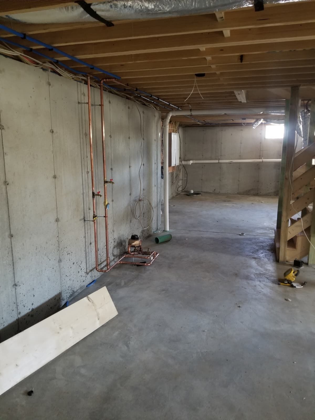 Unfinished basement interior with concrete floor, exposed wiring, and wooden ceiling framing.