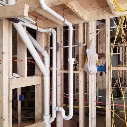 Interior wall framing with white PVC plumbing pipes and exposed studs in a house under construction