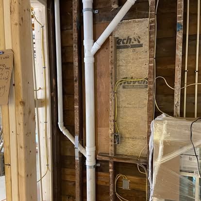 Exposed wall framing with white PVC plumbing pipes and insulation in an unfinished interior wall