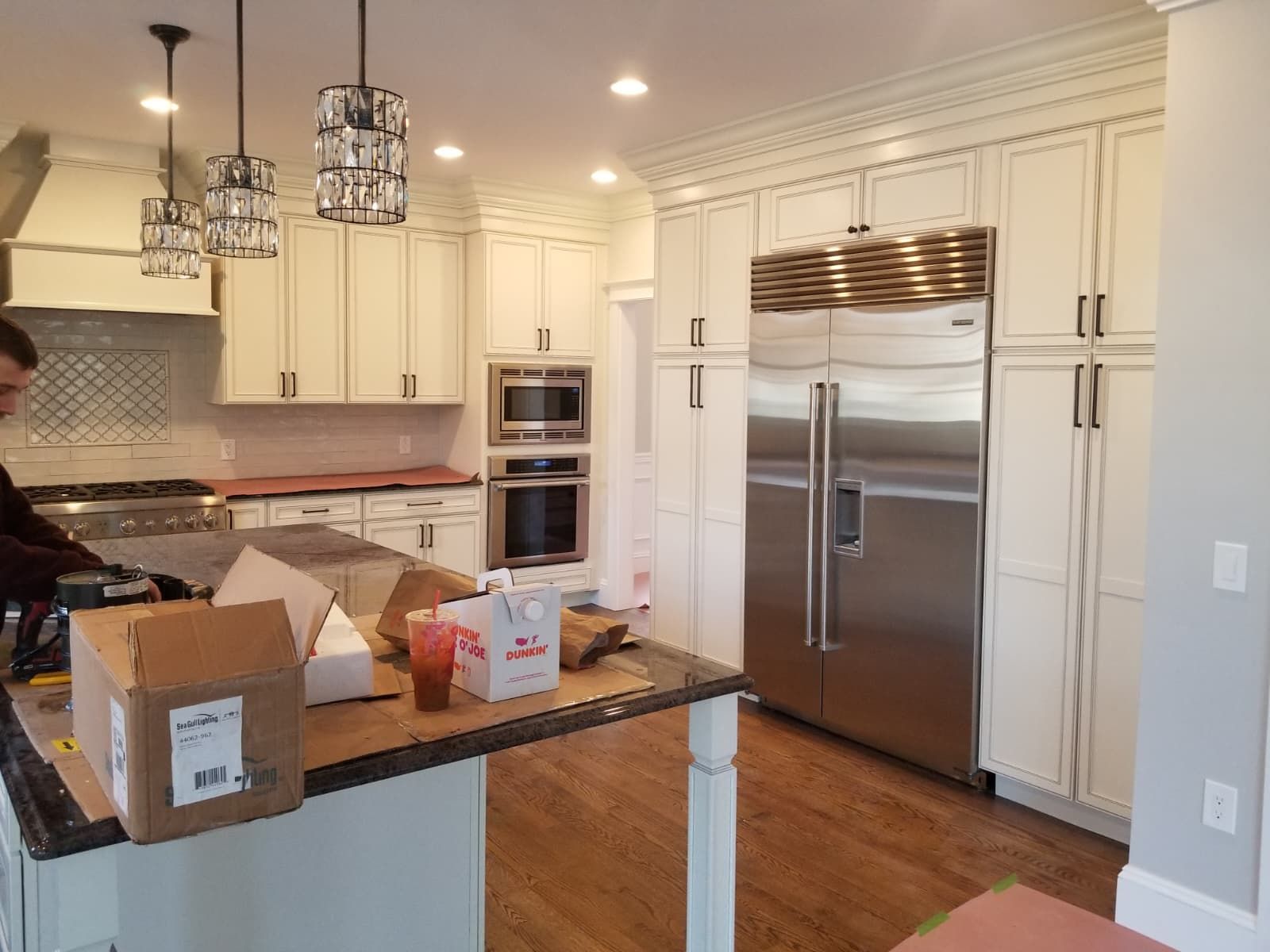 Modern kitchen with stainless steel appliances, white cabinets, granite island, and a person unpacking boxes