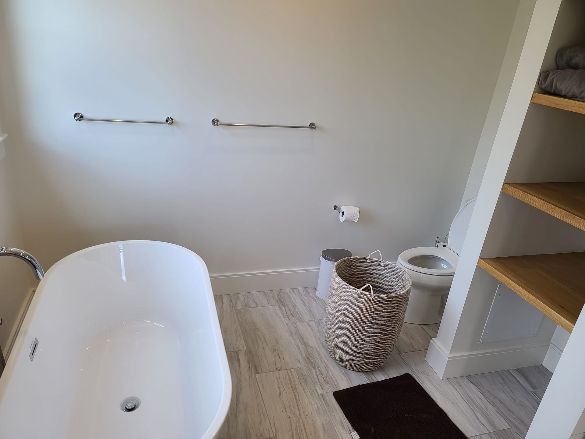Bathroom with a white bathtub, towel bars, woven baskets, and wooden shelves.