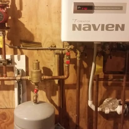 Navien tankless water heater with copper plumbing and a small gray tank in a utility room