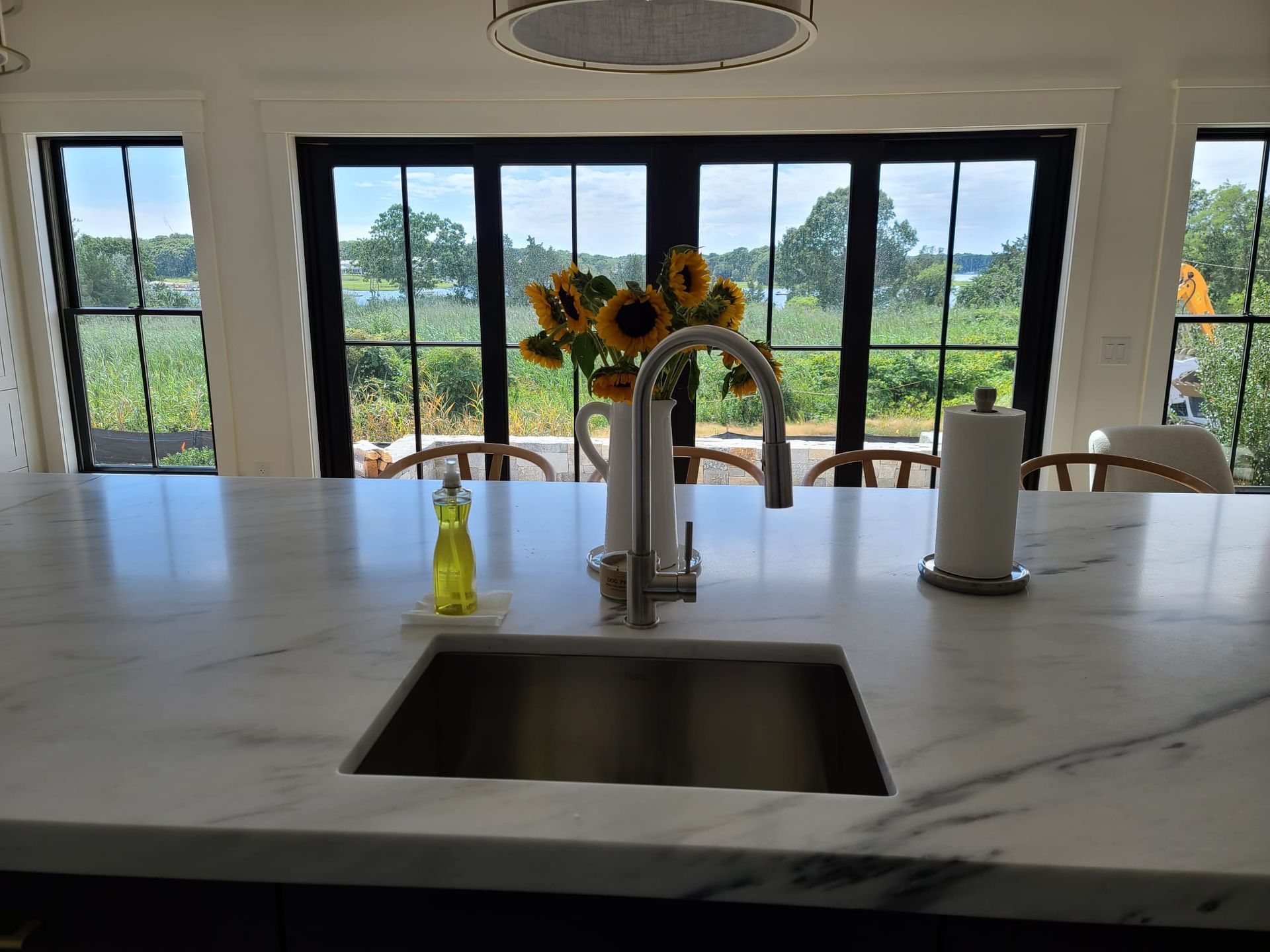 Modern kitchen island with sink, faucet, sunflowers, and large windows overlooking greenery