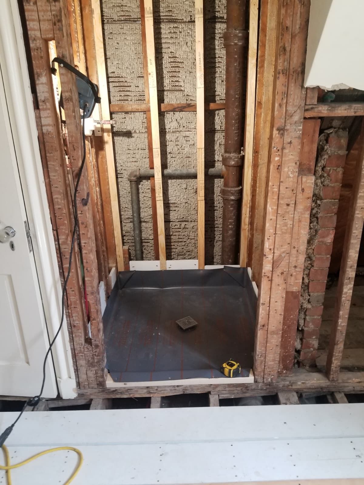 Exposed wall framing and a small tiled shower alcove under renovation, with tools on the floor.