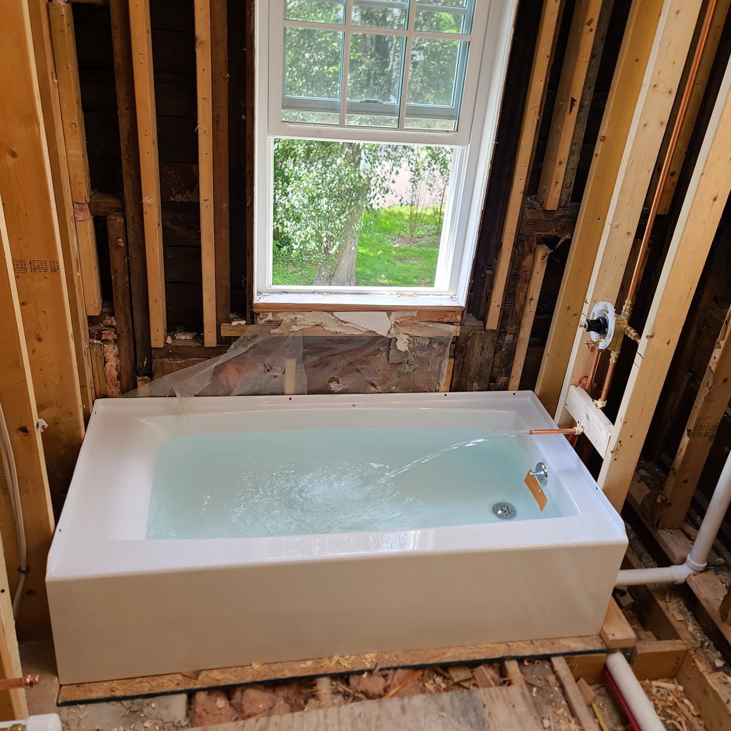 Bathtub installed in an unfinished bathroom with exposed studs and a window view outside.