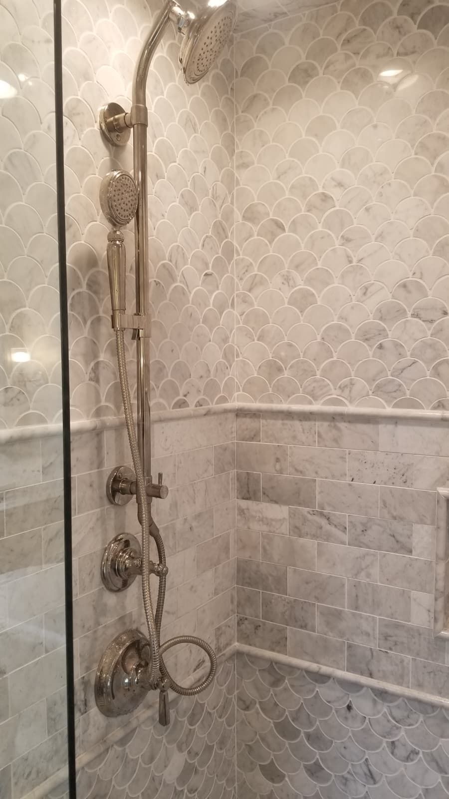 Glass shower with chrome fixtures and gray patterned tile walls