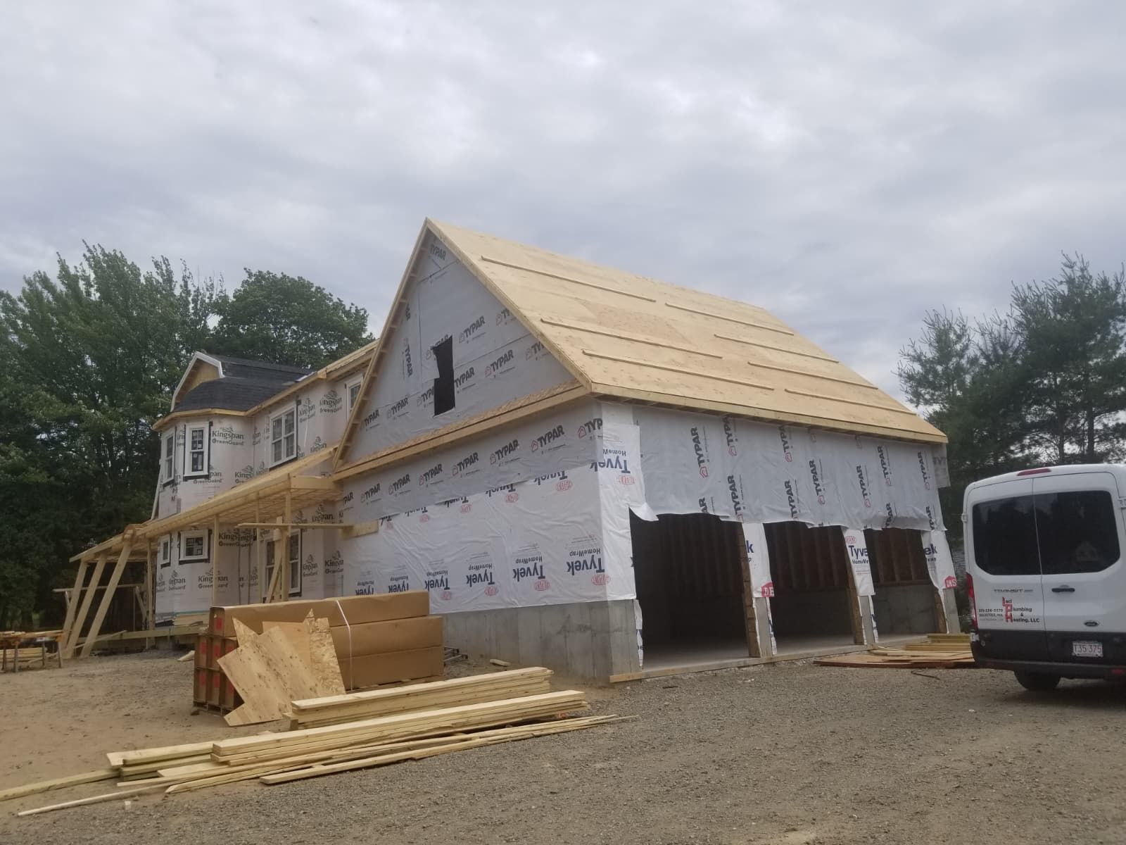 Partially built house with white wrap, exposed roof framing, and construction materials in front