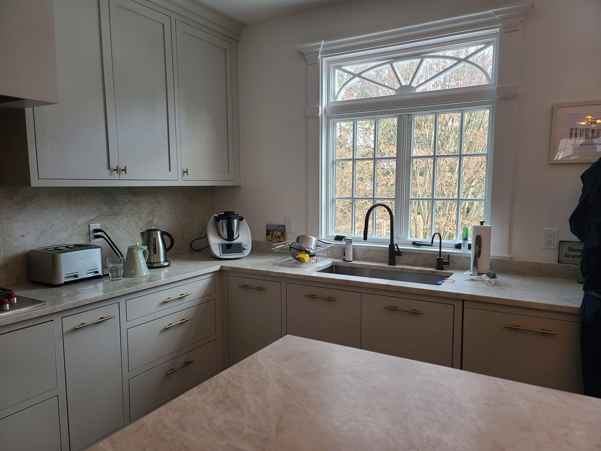 Bright kitchen with white cabinets, large window, countertop appliances, and a table in the foreground
