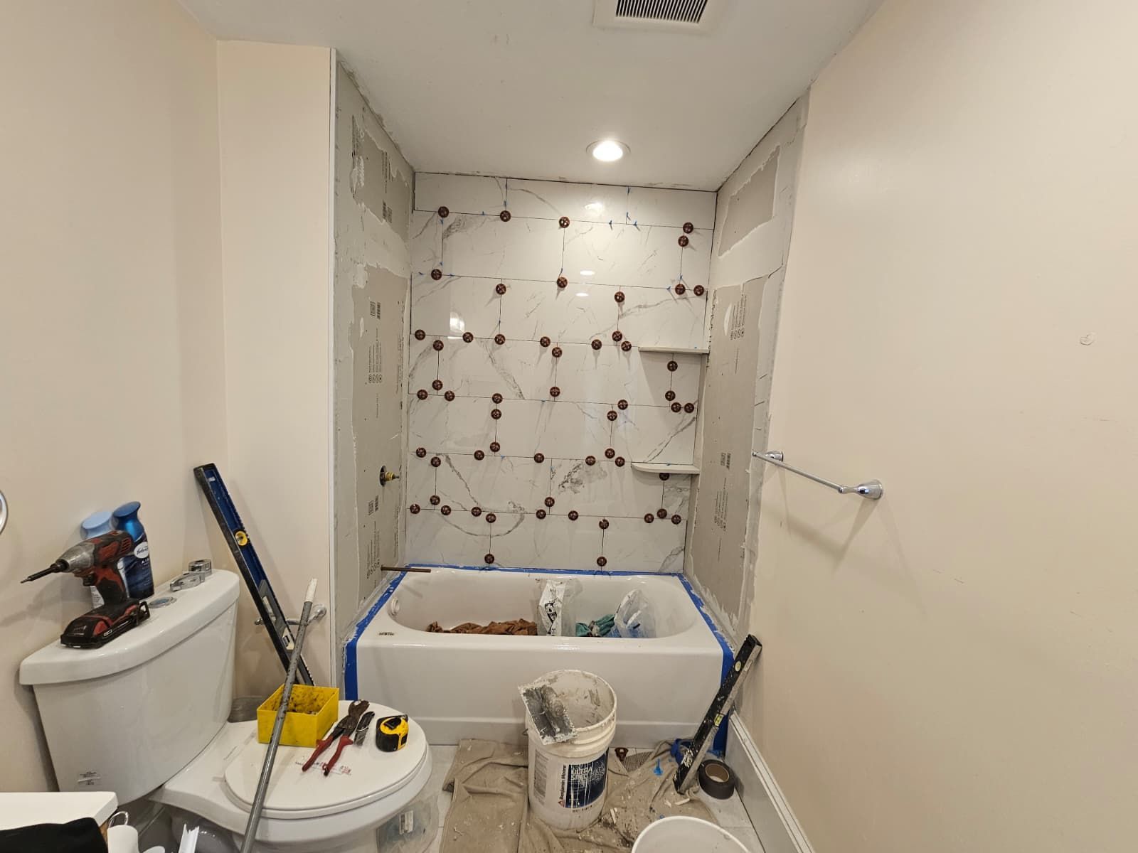 Small bathroom under renovation with tub, tools, and wall tile work in progress
