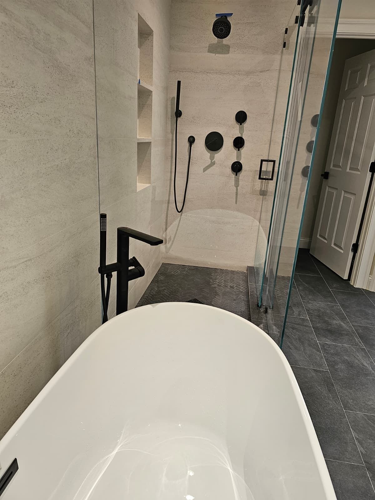 Modern bathroom with freestanding tub, black fixtures, tiled shower, and open glass door
