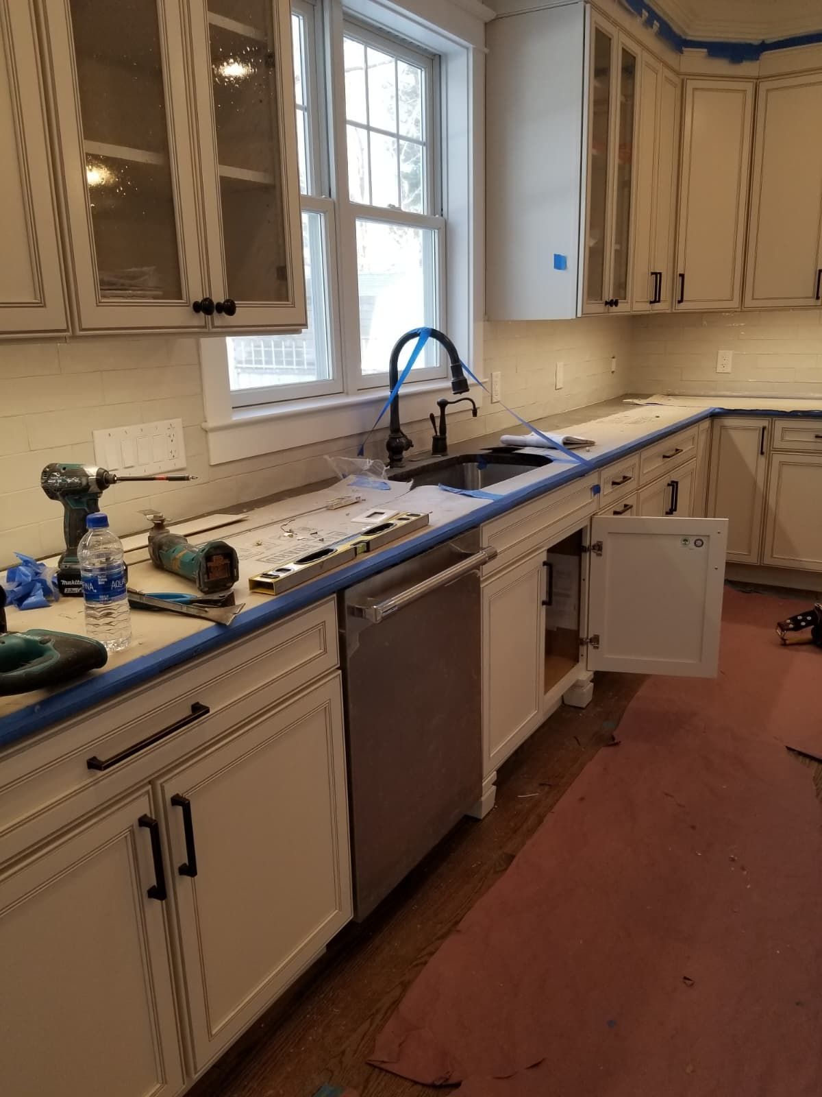 Kitchen under renovation with white cabinets, tools on counter, and a sink by the window