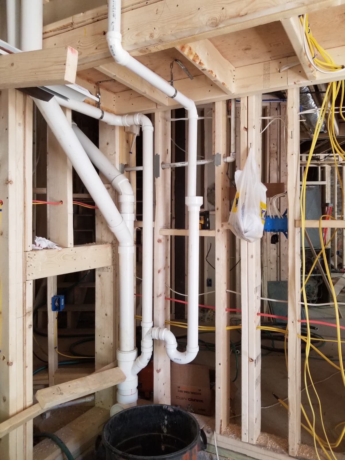 Interior wall framing with white plumbing pipes and exposed electrical wiring in an unfinished house construction area