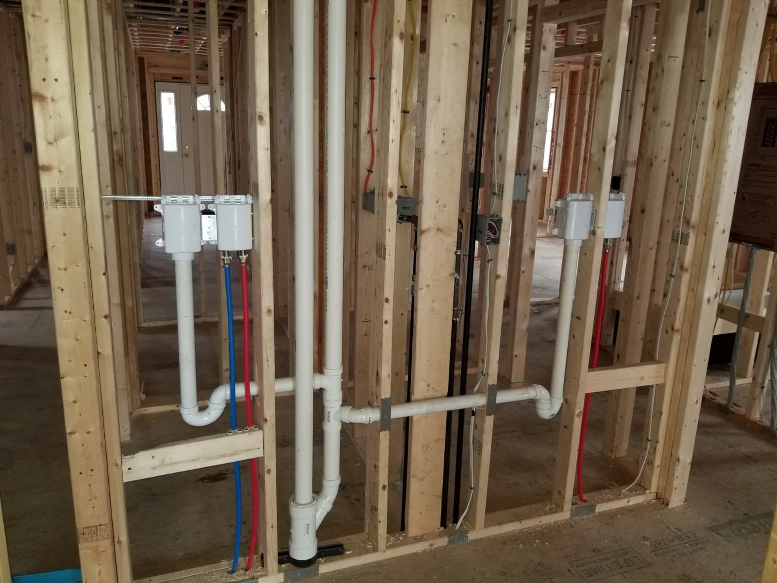 Unfinished wall framing with exposed plumbing pipes and electrical boxes in a house under construction