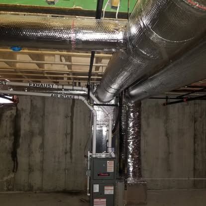 Basement utility room with large silver HVAC ducts and an electrical panel against concrete walls
