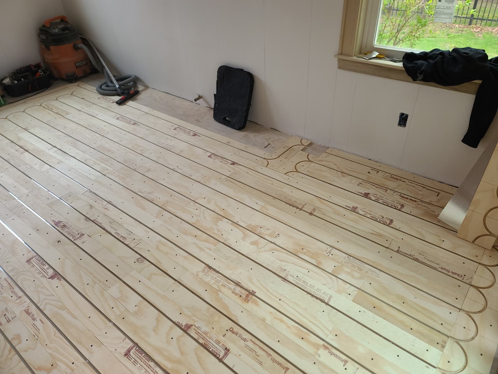 Partially installed wood floor in a room, with tools and supplies near the walls