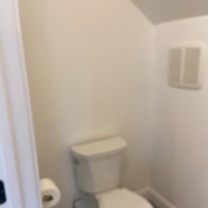 Small bathroom corner with a white toilet, toilet paper holder, and wall-mounted dispenser.