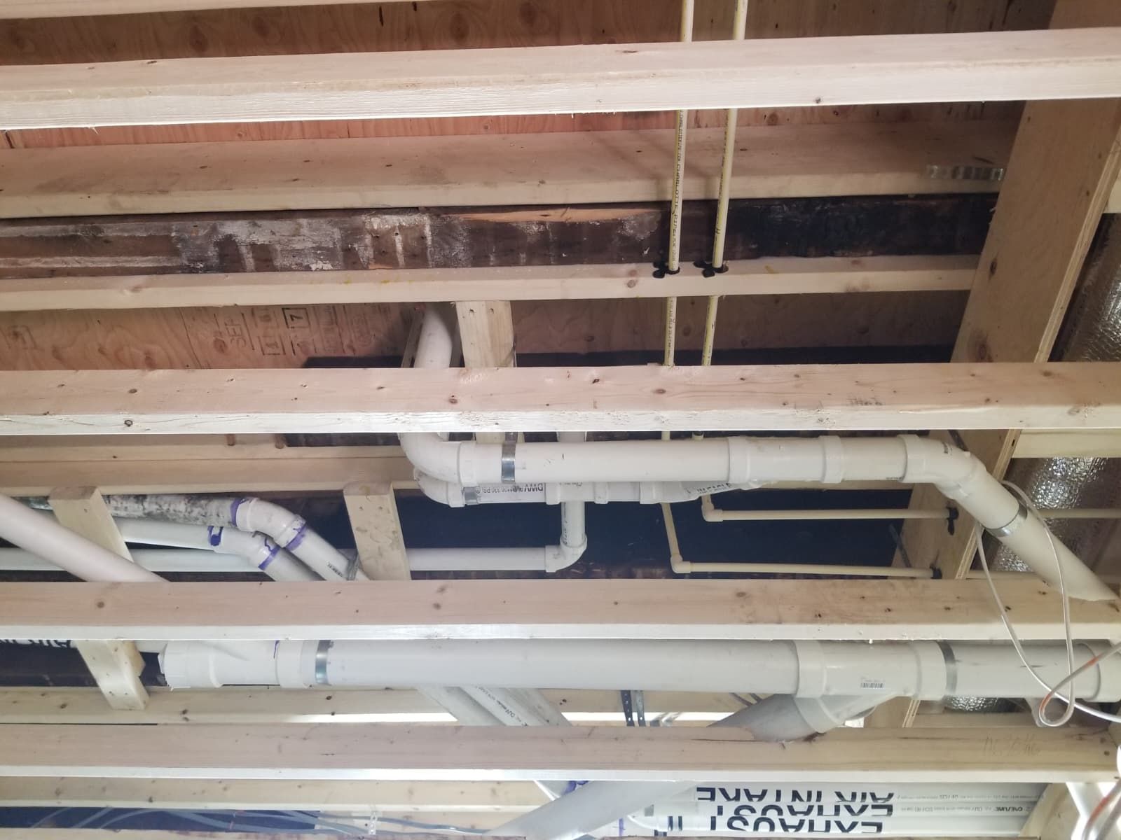 Exposed ceiling joists with white pipes and vents in an unfinished indoor space