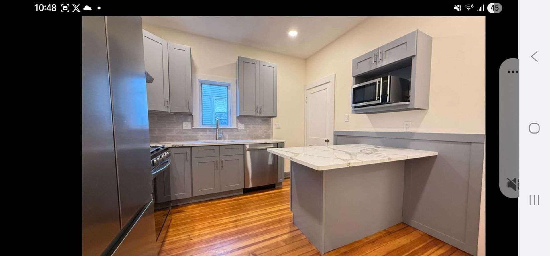 Modern kitchen with stainless steel fridge, white cabinets, island, and wood floors.