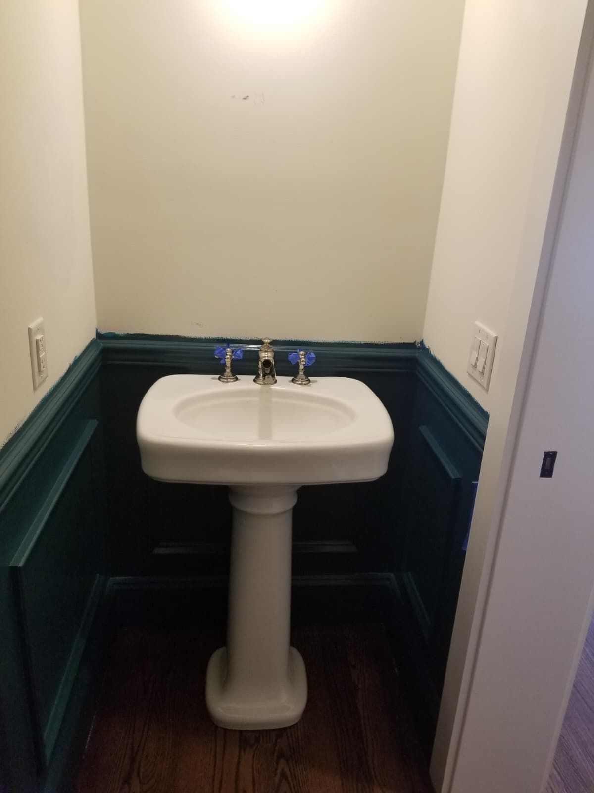 Small bathroom nook with a white pedestal sink and teal wainscoting.