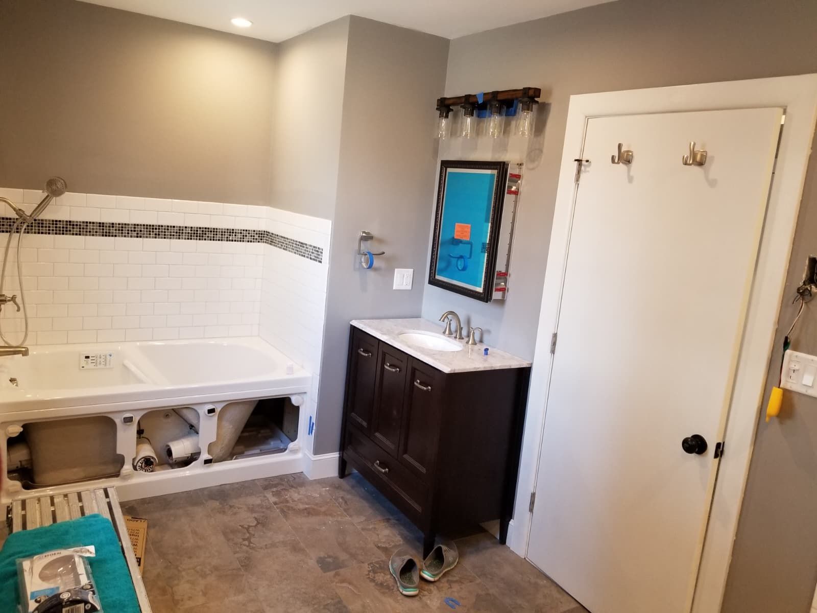 Bathroom under renovation with a tub, vanity, white door, and exposed wall opening by the sink.