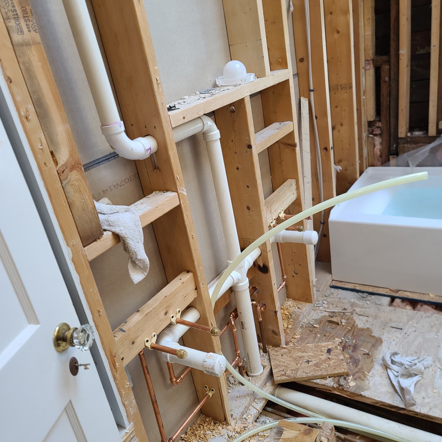Exposed bathroom wall framing with plumbing pipes and a white tub during renovation