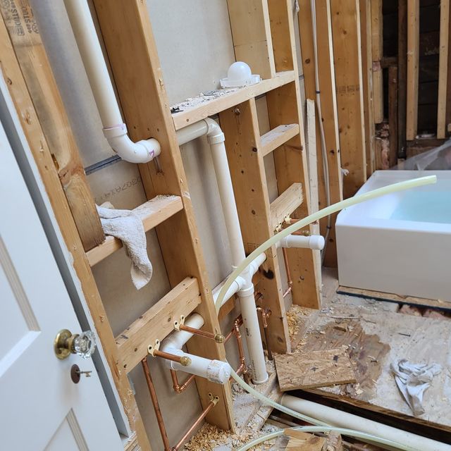 Exposed bathroom wall framing with white plumbing pipes and a shower tub edge during renovation