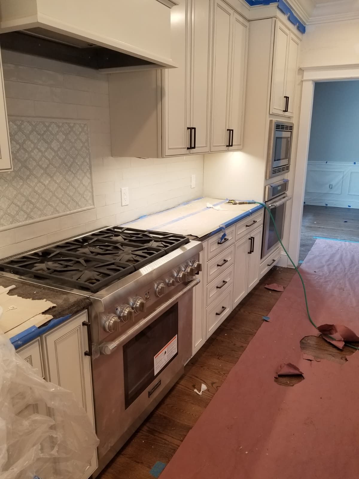 Kitchen under renovation with white cabinets, blue painter’s tape, and a stainless steel stove