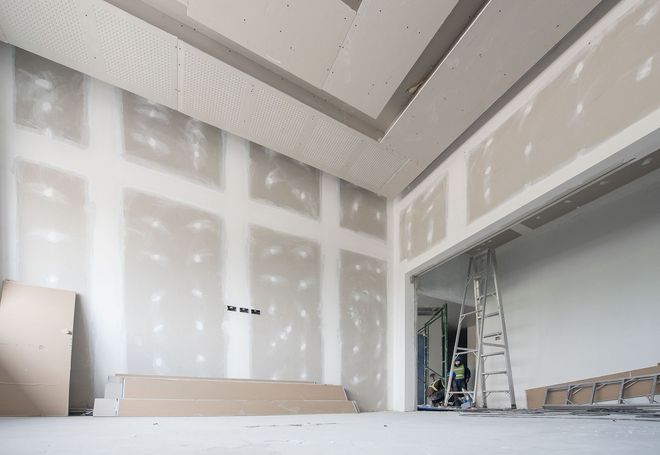 Unfinished interior room with installed drywall, tape-covered joints, and a ladder visible in an open doorway.