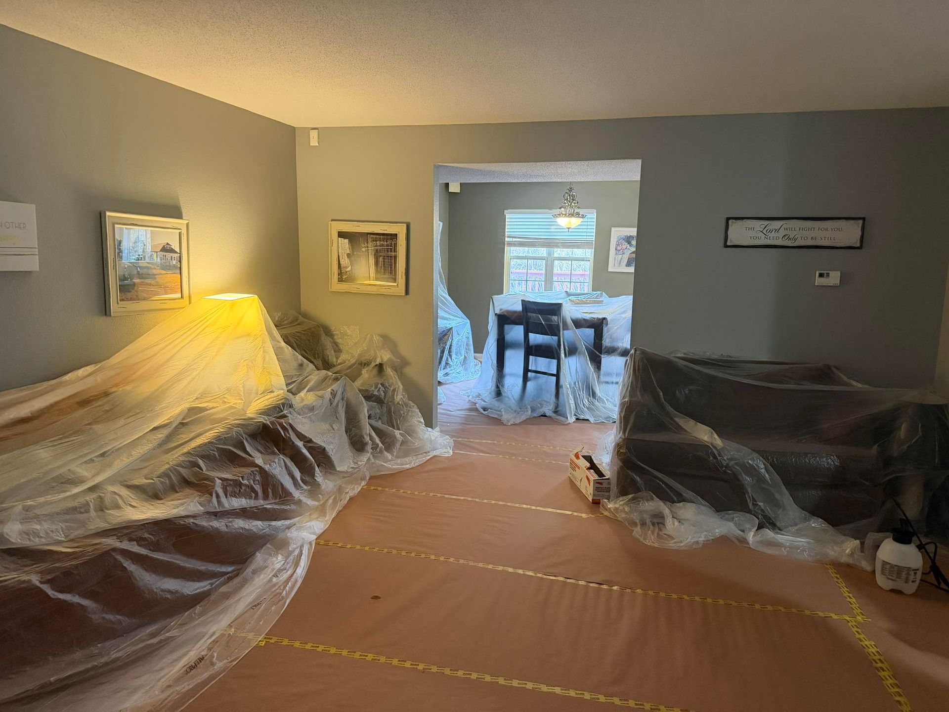 Interior of a room being painted, furniture and floors covered in plastic sheeting.