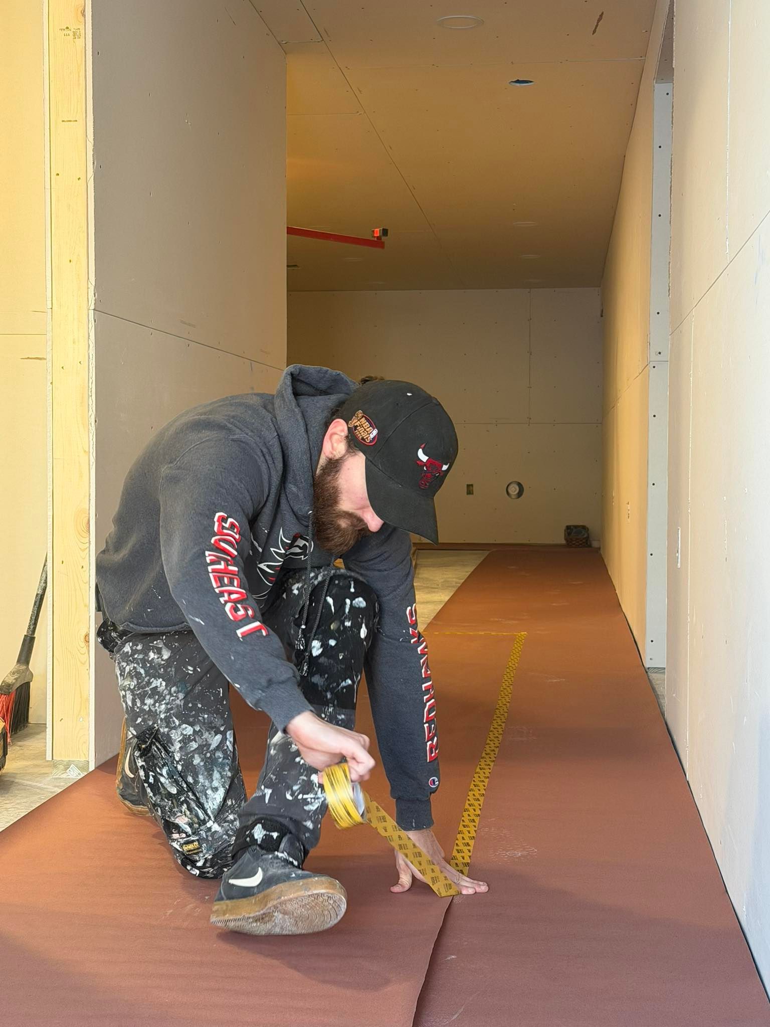 Person kneeling, measuring flooring in a construction hallway with a measuring tape.