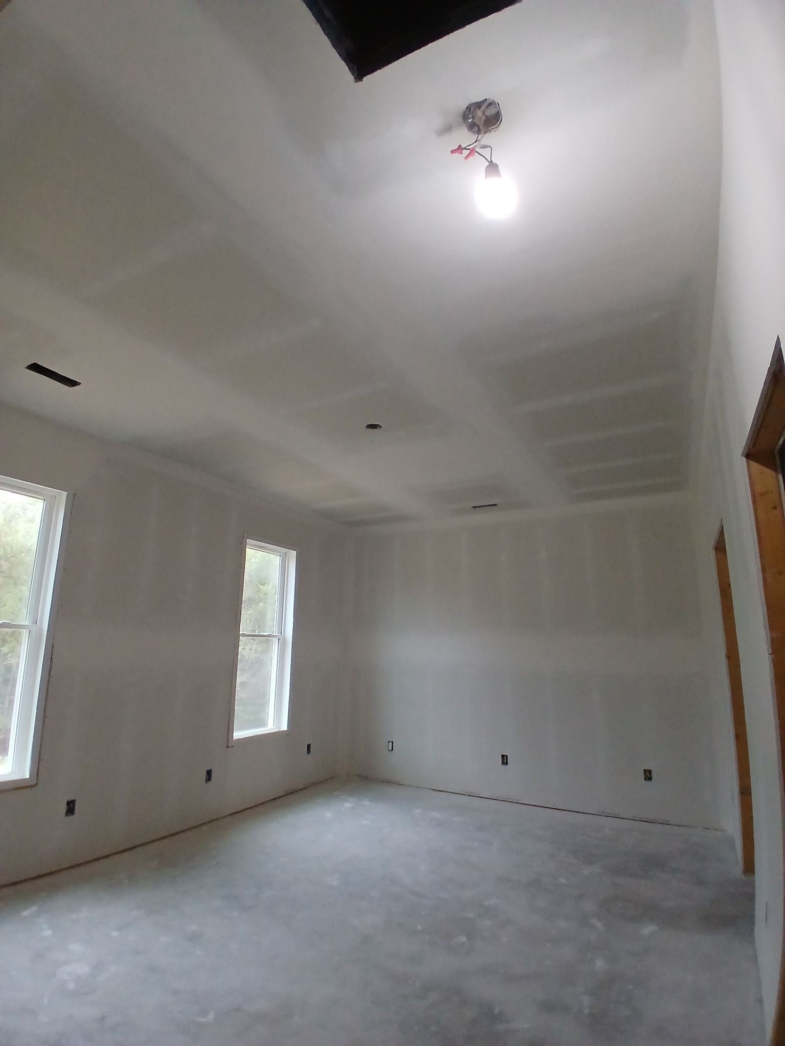 Unfinished room with drywall walls and ceiling, concrete floor, windows, and exposed light fixture.