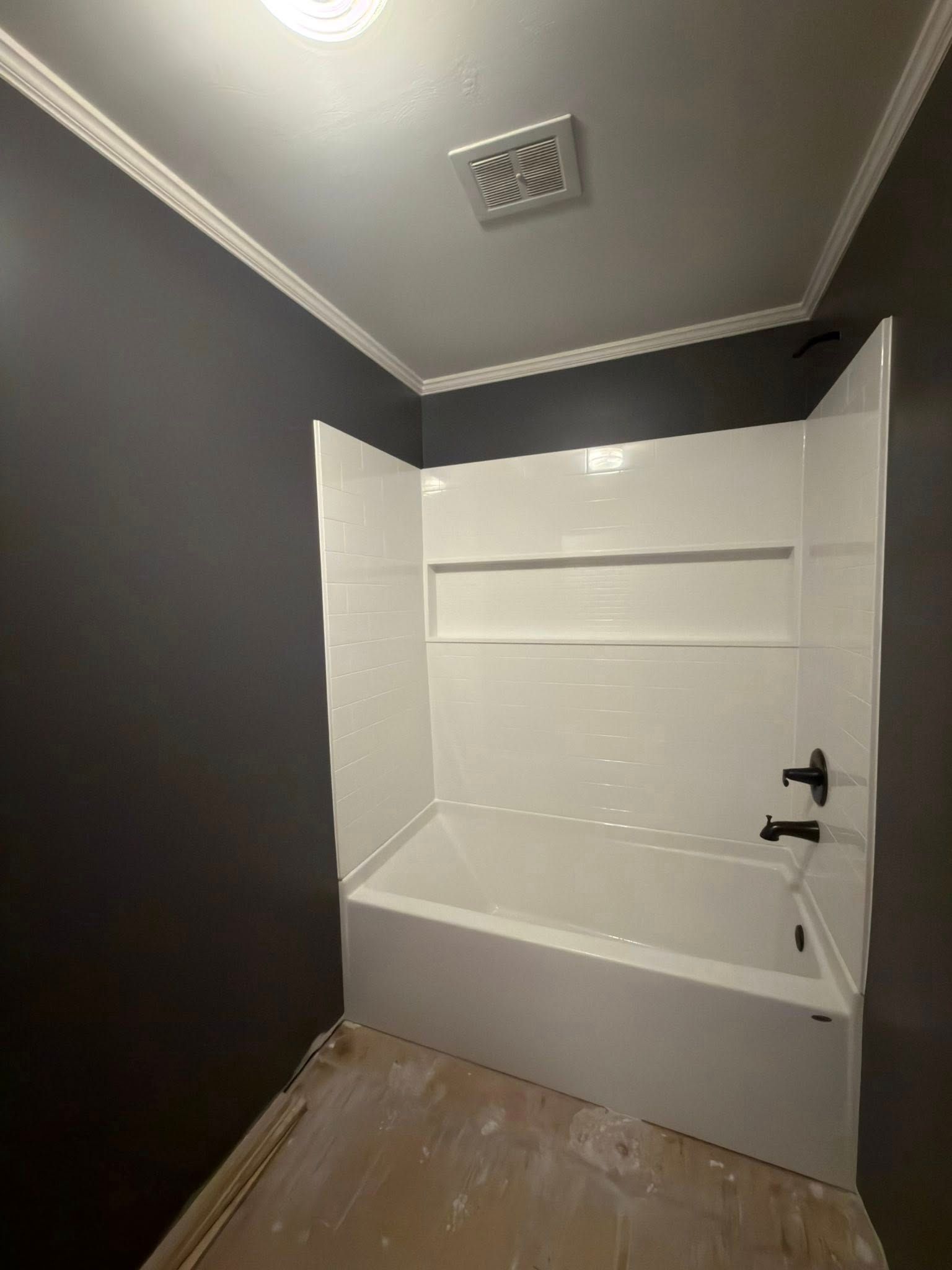 Bathroom with white tub and surround, dark gray walls, and white trim.