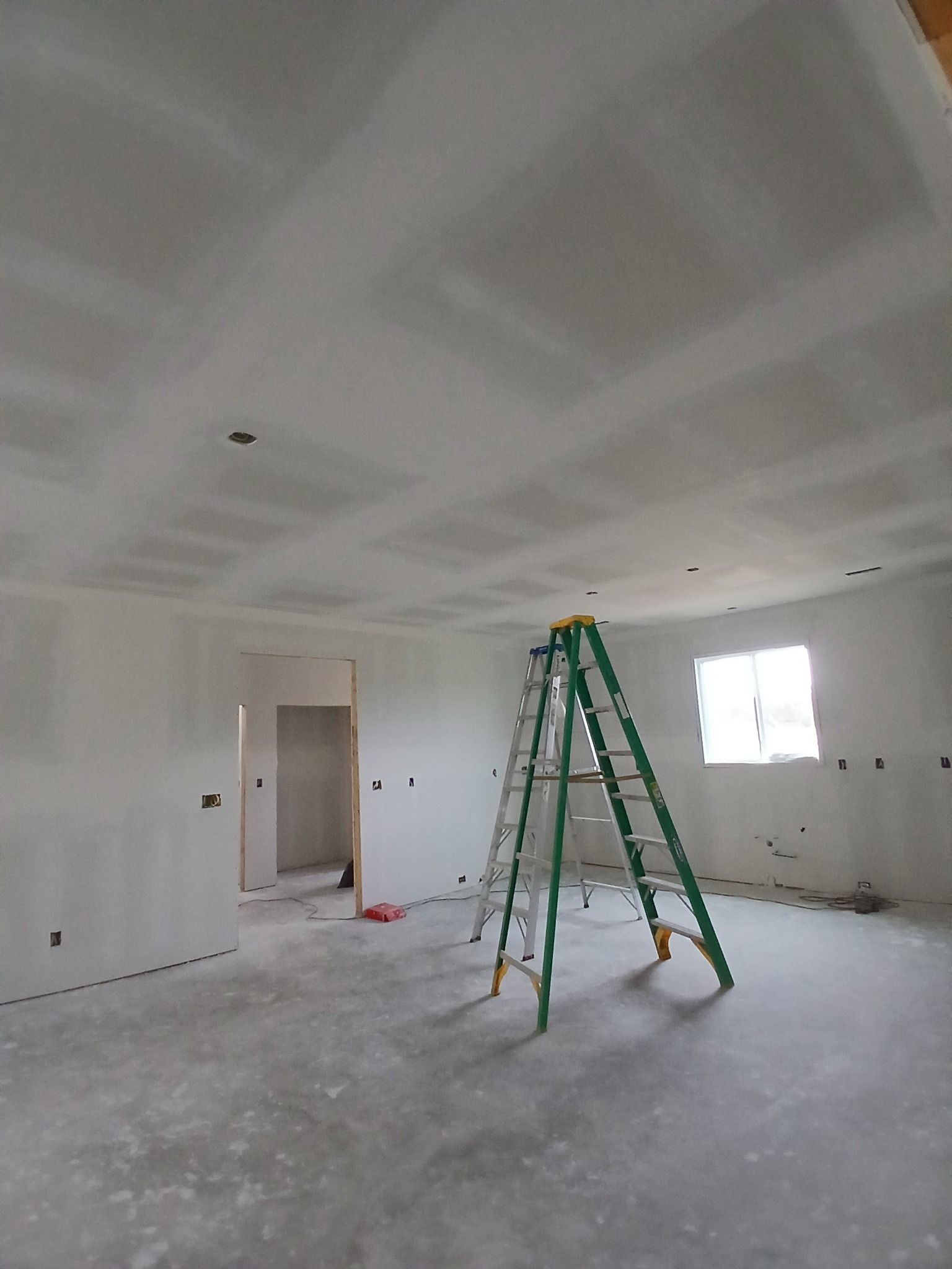 Interior of a room under construction with drywall on the walls and ceiling, a ladder, and a doorway.