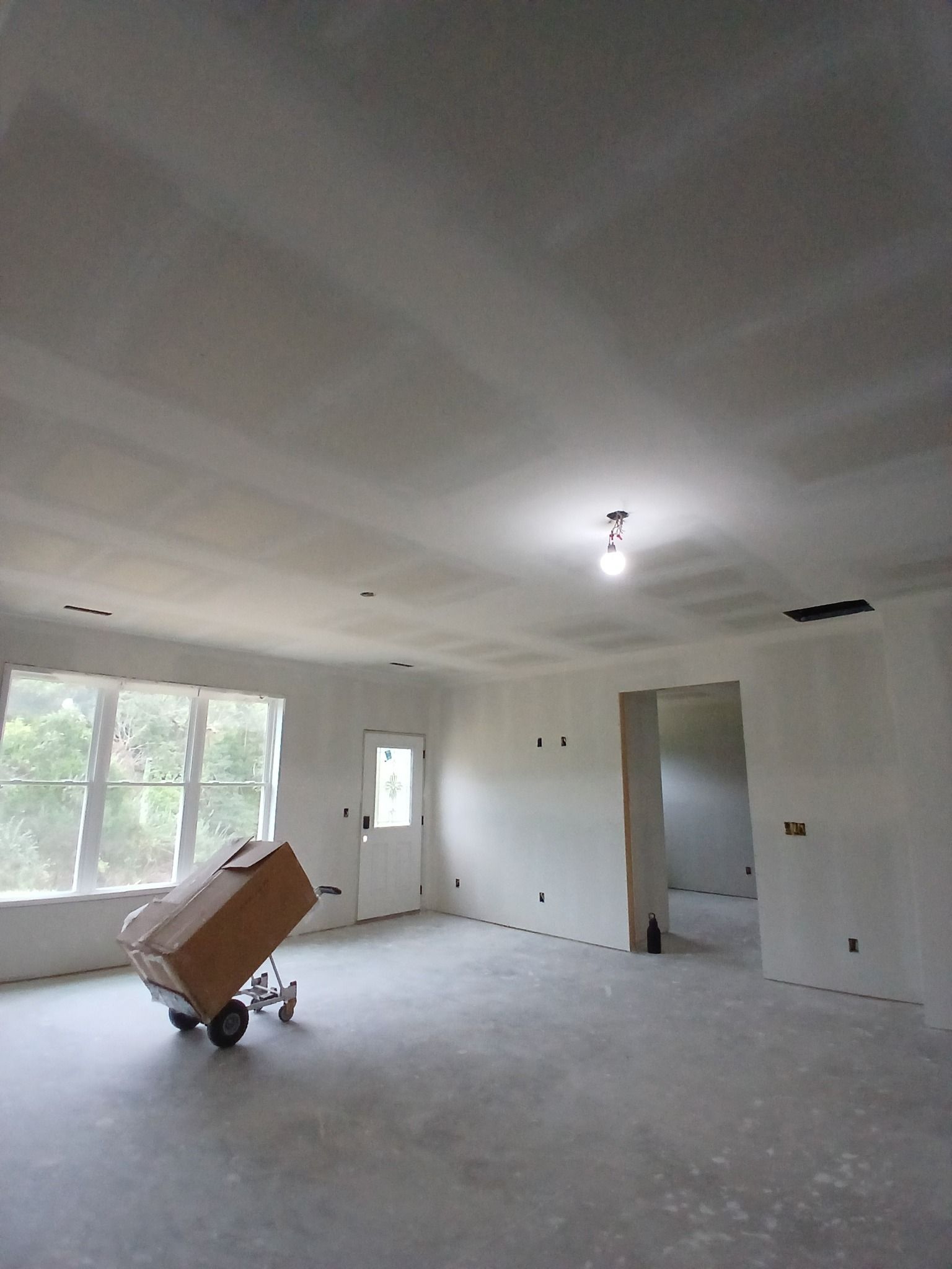 Interior view of a room under construction with exposed drywall and a box on a cart.