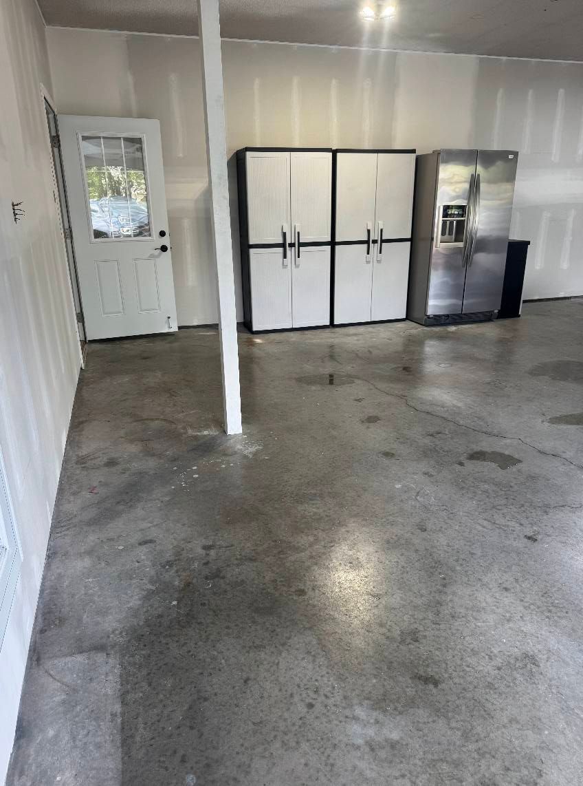 Garage interior with concrete floor, white storage cabinets, and a white door.