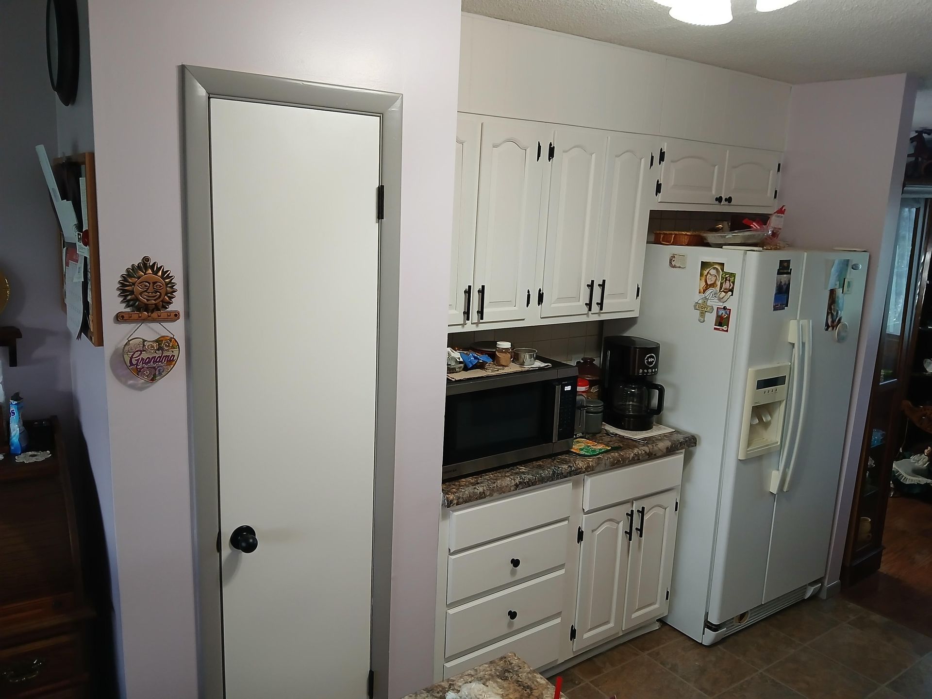 Kitchen with white cabinets, appliances, microwave, and a pantry door.