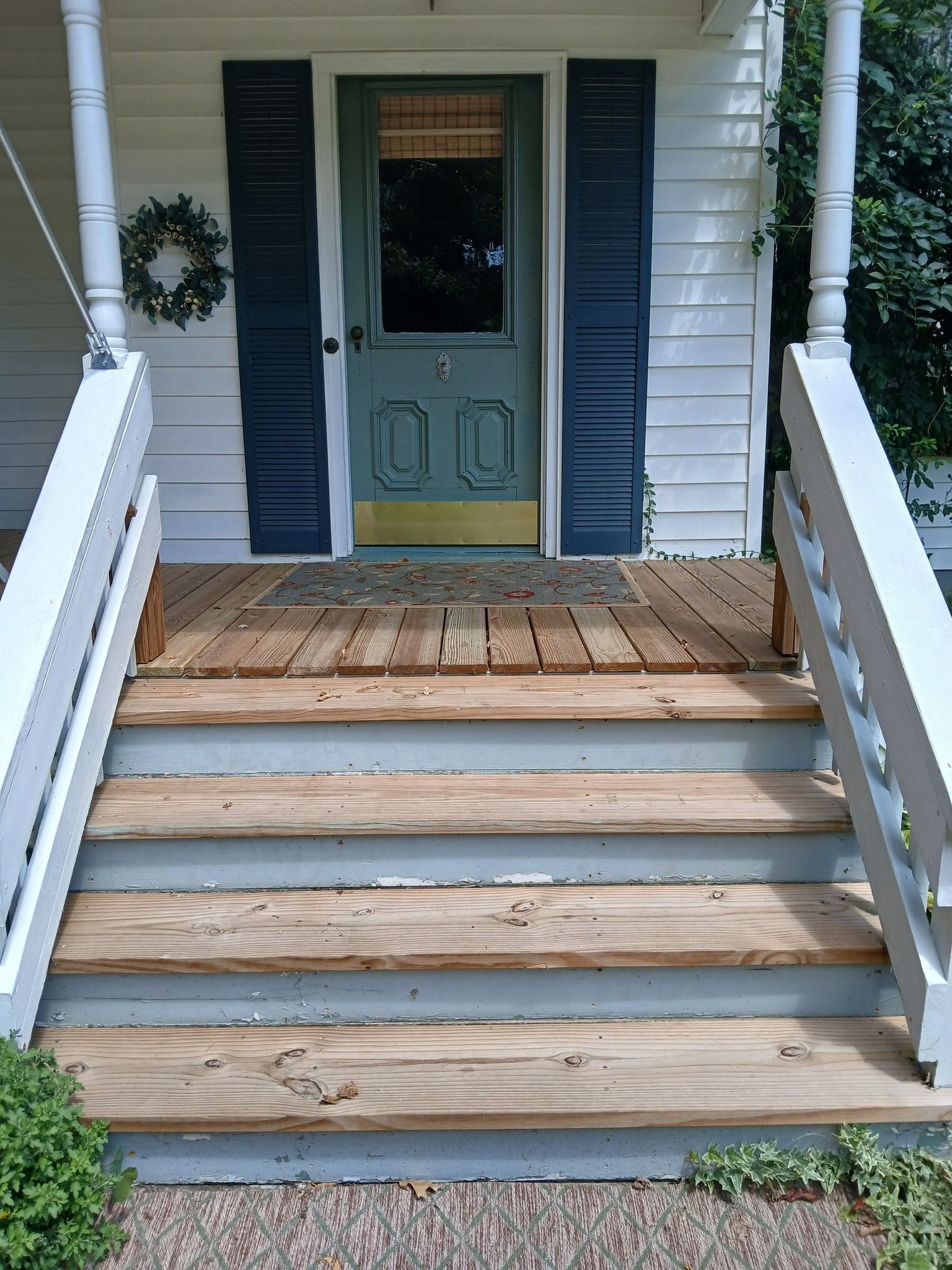 Front porch with weathered wooden steps leading to a green door with dark blue shutters.
