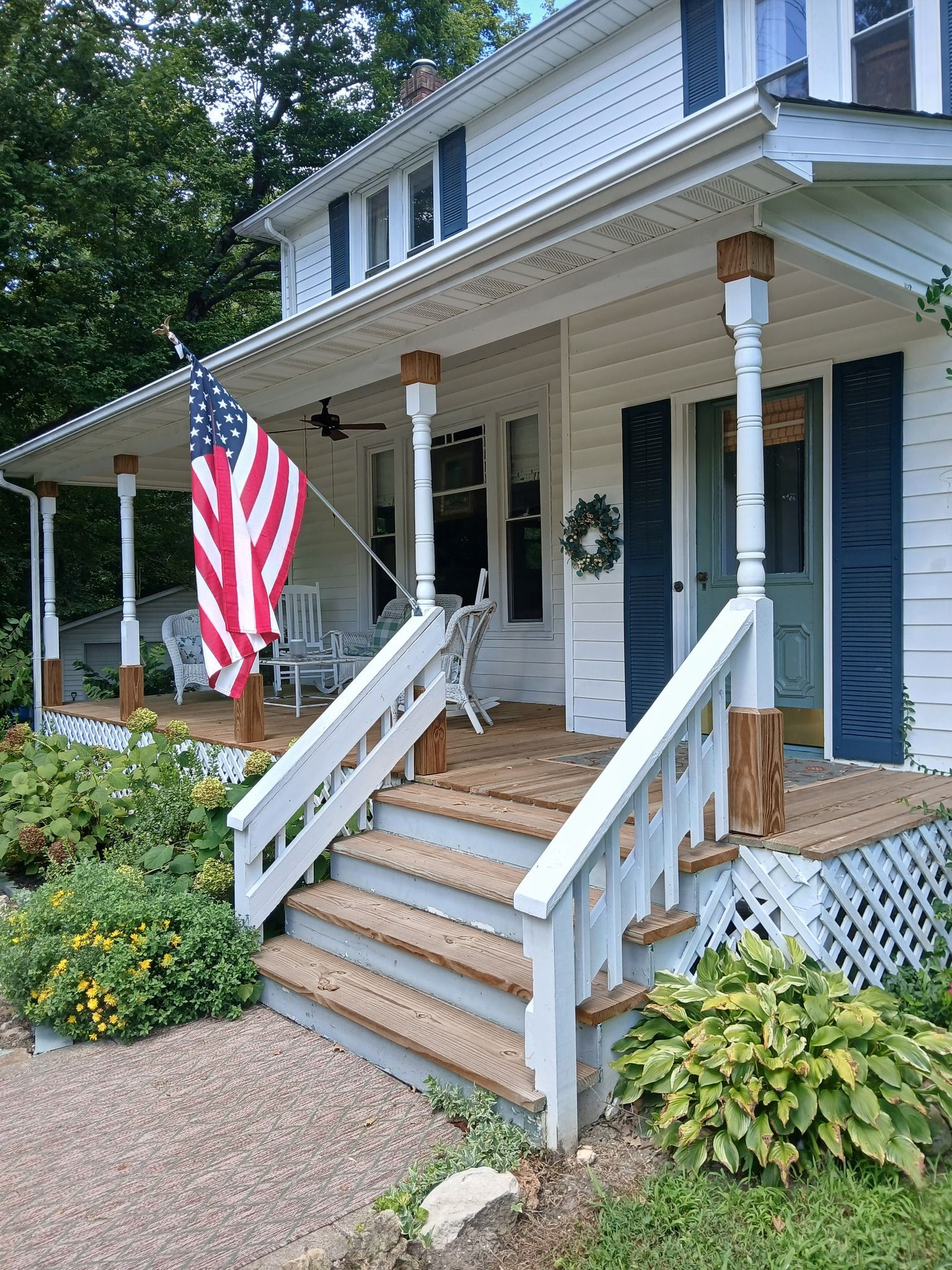 A two-story white house with a porch, American flag, and steps leading up.