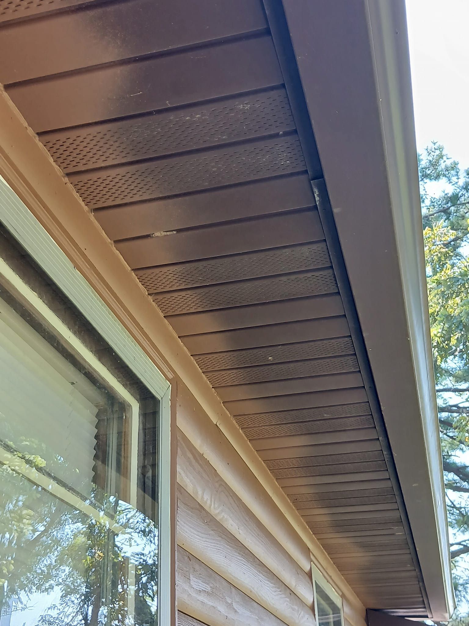 Brown soffit and siding with ventilation holes near a window.