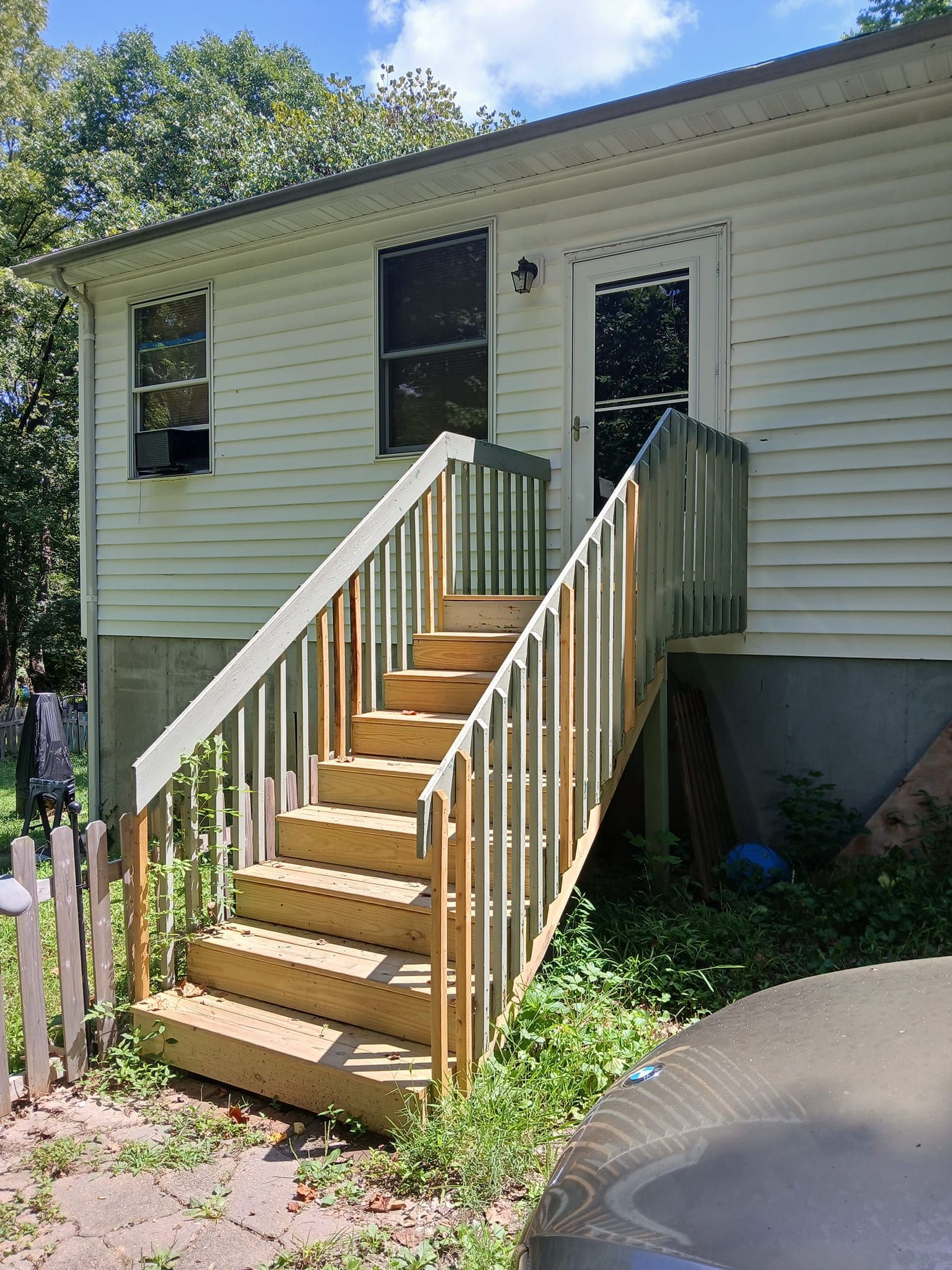 Wooden stairs leading up to a house's back door. The house has white siding, a window, and a door with glass panels.