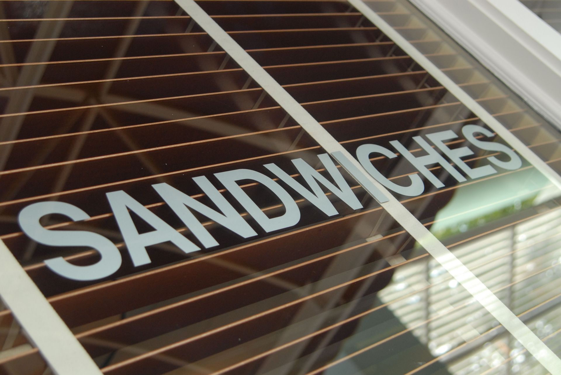 White “SANDWICHES” sign on a shop window with closed blinds behind it